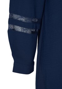 Manche de chemise bleu marine avec un panneau en dentelle à motifs floraux et deux bandes horizontales, terminée par un bord à revers.