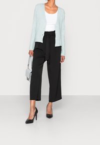 Cardigan azzurro chiaro a coste con bottoni, abbinato a pantaloni a gamba larga neri e décolleté neri; una piccola borsa grigia completa l'outfit.