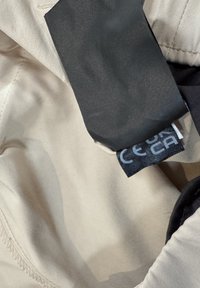 Beige fabric with visible stitching and attached black fabric label showing partial CE mark and text.