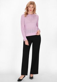 Hellpurpurner Strickpullover mit Diamant- und Zickzackmustern, kombiniert mit schwarzen weit geschnittenen Hosen und schwarzen Schuhen.