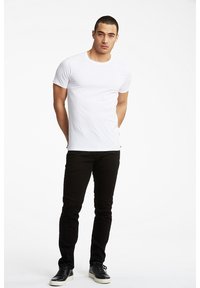 Valkoinen lyhythihainen t-paita, jossa on pyöreä kaula-aukko, yhdistettynä slim-fit mustiin farkkuihin ja mustiin lenkkareihin, joissa on valkoiset pohjat. Yksinkertainen muotoilu, istuva malli.