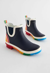 Stivali in gomma blu navy con rifiniture bianche, dettagli arcobaleno sul tallone e sulla suola, e una fodera accogliente. Presentano un logo sulla parte anteriore.