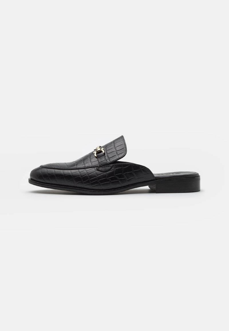 Mocassin noir en cuir à enfiler avec texture crocodile et détail boucle métallique dorée, talon bas et bout pointu.