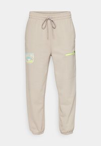 Beige Jogginghose aus weichem Material, mit elastischem Bund und Kordelzug, seitlicher Reißverschlusstasche und geprägtem Logodetail.