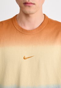 Nike marškinėliai su perėjimu nuo smėlio iki oranžinės, su mažu išsiuvinėtu oranžiniu logotipu krūtinėje, pagaminti iš švelnaus medvilninio audinio.