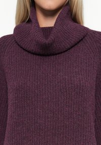 Pull en tricot violet avec un col haut et replié, texture côtelée et manches larges, mettant en valeur un tissu doux et chaud.