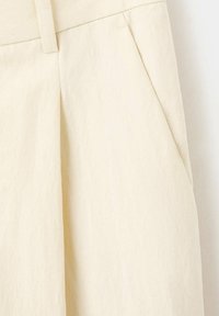 Pantalon beige taille haute avec passants pour ceinture et poche sur la couture latérale, en tissu texturé.