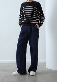 Svart och vit randig stickad tröja med vida ärmar, parat med löst sittande mörk denimbyxor och vita sneakers. Enkel design och textur.