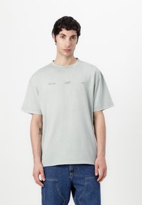 Grijze oversized t-shirt van zachte stof met een ronde halslijn en korte mouwen; is voorzien van minimalistische logo's die op de voorkant zijn gedrukt.