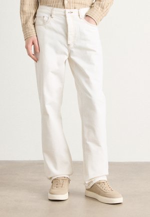Hvite rette jeans med kontrastsøm, med frontlommer og knappelukking. Kombinert med beige sneakers.
