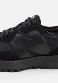 Schwarzer Sportschuh mit einem strukturierten Leder- und Mesh-Obermaterial, einem auffälligen "N"-Logo und einer geformten Gummisohle für Traktion.