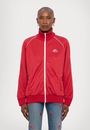 Rød zip-up jakke med høj krave, hvide piping detaljer og to frontlommer. Båret med jeans med jordbærmønster.