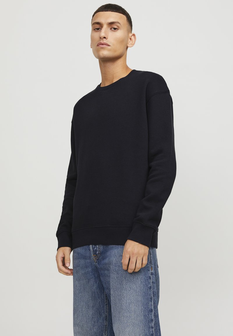 Sudadera de color azul marino oscuro, hecha de un tejido suave, con cuello redondo, mangas largas y puños acanalados. Se combina con unos vaqueros de mezclilla azul claro.