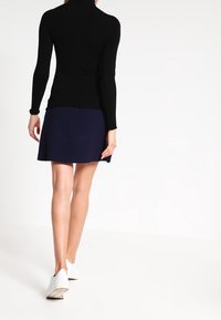 Haut noir à manches longues avec col montant associé à une jupe évasée bleu marine. Des baskets blanches complètent la tenue, mettant en avant un style décontracté.