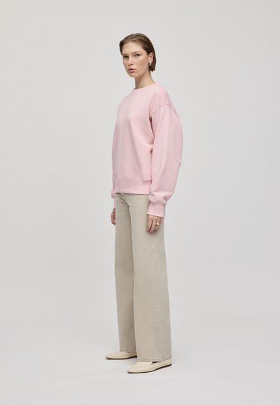 Felpa rosa chiaro con spalle scese, abbinata a pantaloni beige a vita alta con gamba larga e scarpe basse beige. Design semplice e senza soluzione di continuità.