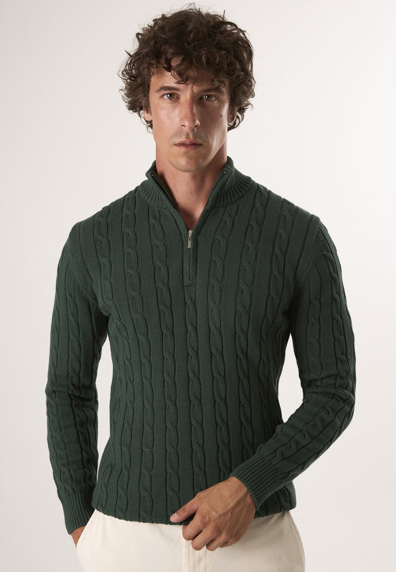 Dunkelgrüner Pullover mit hohem Kragen, halbem Reißverschluss und einem Zopfmuster-Design sowie gerippten Bündchen und Saum. Angenehme, glatte Textur.