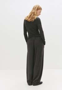 Donkergrijze, langemouwen top en wijde broek, gemaakt van zachte stof. Heeft een elastische taille en een relaxte pasvorm, met een gladde textuur.