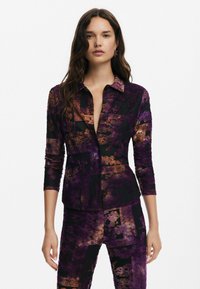 Camicia con bottoni e maniche lunghe, caratterizzata da un motivo astratto viola e nero con dettagli bronzo. Realizzata in tessuto morbido con colletto.