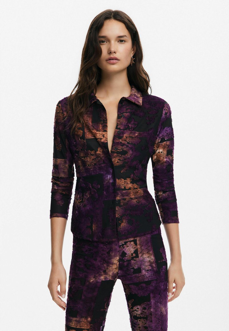 Camicia con bottoni e maniche lunghe, caratterizzata da un motivo astratto viola e nero con dettagli bronzo. Realizzata in tessuto morbido con colletto.