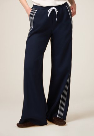 Navy wide-leg pants featuring a drawstring waist, side stripes in white, and a soft texture, providing a relaxed fit and style.