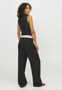 Svart ärmlös topp med en åtsittande design och en sprund i ryggen, ihopparad med vida svarta byxor och en kontrasterande vit midjeresår.