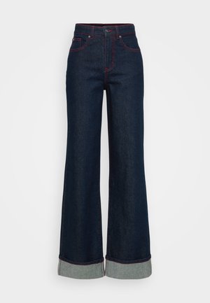 Mørkeblå vidde jeans med oppbrettede hem og synlig rød søm på lommer og sømmer, med knapp og glidelås.