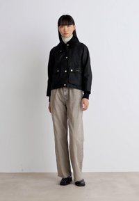 Zwarte cropped jack met twee voorzakken, knoopsluiting en geribbelde manchetten. Gecombineerd met lichtgrijze broeken en zwarte schoenen.