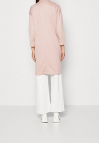 Vaaleanpunainen, pitkähihaisen tunikan, jossa on käännettävät hihansuut; polvipituinen; yhdistetty leveälahkeisiin valkoisiin housuihin ja kulmikkaisiin valkoisiin korkokenkiin. Yksinkertainen malli.