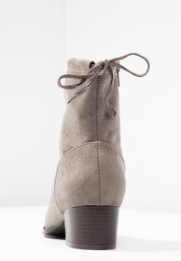 Šedá zamšová kotníková bota s kulatou špičkou, zadním šněrováním a nízkým zvýšeným podpatkem. Hladká textura a jednoduchý design s minimálními detaily.