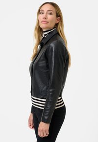 Zwarte leren jack met een iets cropped ontwerp, voorzien van een klassieke kraag en een gestreepte ribgebreide zoom. Glad van textuur en getailleerde pasvorm.