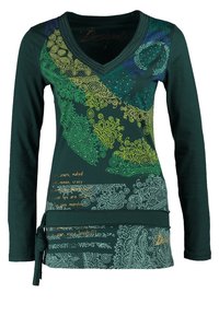 T-shirt vert à manches longues avec un col en V, featuring des motifs tourbillonnants colorés et des designs textuels. Accent à la taille nouée pour la forme. Matériau en coton doux.