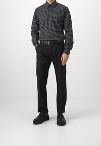 Camicia a maniche lunghe nera con motivo, abbinata a pantaloni neri su misura e scarpe nere. La camicia presenta un design geometrico.