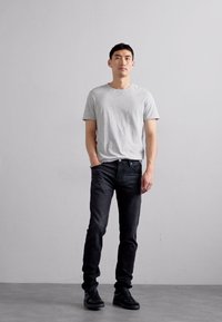 Grå bomulls t-shirt i kombination med svarta denimjeans och svarta sneakers. Passformen är avslappnad, med en standard rund halsringning och en stilren design.