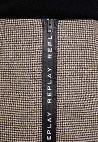 Brun och beige hundtandsmönstrad kjol med svart dragkedja och texten "REPLAY" längs sidan. Texturerad tygfinish.