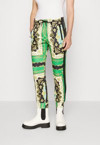 Pantalones de chándal con un patrón en colores verde, negro y blanco con acentos dorados. Incluyen una cinturilla elástica y bolsillos laterales.