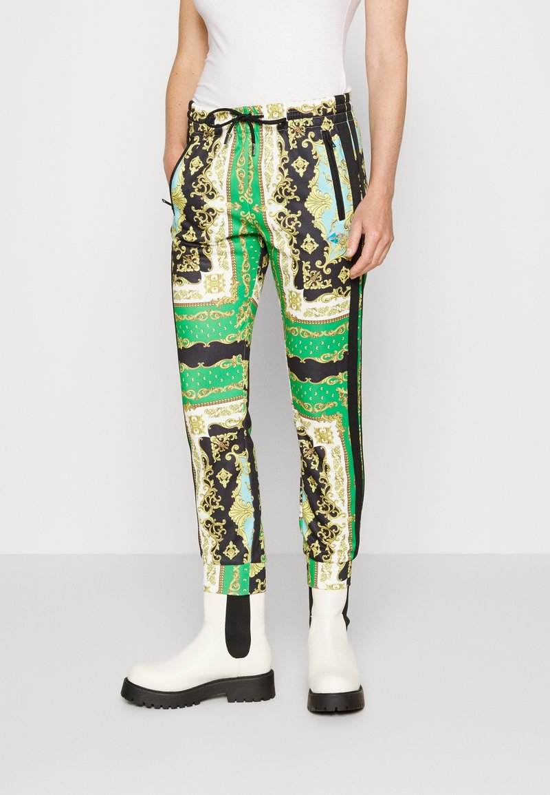 Pantalones de chándal con un patrón en colores verde, negro y blanco con acentos dorados. Incluyen una cinturilla elástica y bolsillos laterales.