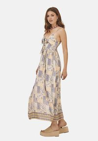 Vestido maxi de tejido ligero con un patrón de patchwork en amarillo, azul y blanco. Presenta un detalle de lazo en la parte delantera y tirantes finos ajustables.