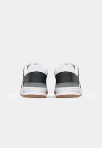 Black and white athletic shoes with a rubber sole, padded collar, and gray accents. Smooth surface with a textured back panel and logo detail.