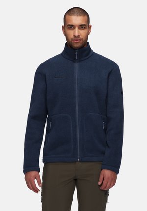 Navy fleece jacket with a high collar, full front zipper, and two side pockets. Features subtle logo detail on the chest and textured fabric.