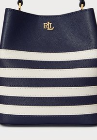 Bolsa listrada em azul-marinho e branco, em material texturizado, com um detalhe de logótipo dourado. O design é estruturado com uma forma suave de balde.