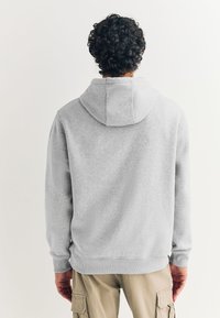 Sweat-shirt gris à capuche, avec une coupe décontractée, des poignets et un ourlet côtelés. Texture douce, coutures discrètes, sans ornements.