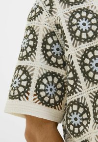 Kvačkana majica z zapletenimi cvetličnimi vzorci v olivno zeleni in svetlo modri barvi na kremnem ozadju, s kratkimi rokavi in teksturiranim dizajnom.