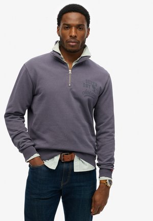 Paarse sweatshirt met rits en geribbelde manchetten, met een logo-opdruk aan de voorkant. Draag het over een lichtgestreept shirt en in combinatie met donkerblauwe jeans.