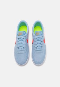 Blaue Wildledersneaker mit einer weißen Sohle, versehen mit einer neongrünen Einfassung und roten Akzenten. Schnürverschluss und Logodetail auf der Zunge.