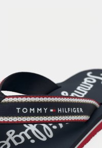 Chancla de color azul marino de Tommy Hilfiger con detalles de tiras en blanco, rojo y beige, y texto del logo en la tira y en la suela.