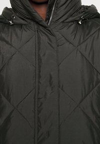 Giubbotto trapuntato verde scuro con cappuccio, motivo di cuciture diagonali, chiusura con zip e particolari con cordino nella zona del cappuccio.