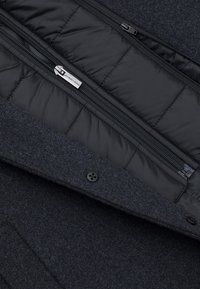 Wnętrze ciemnoszarej wełnianej kurtki z czarną wyściełającą podszewką, z dwoma zamkami błyskawicznymi i zapięciem na guzik. Gładka tekstura i stylowy design.