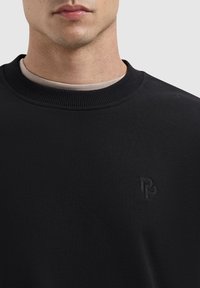 Zwarte sweatshirt met geribde halslijn, met subtiele logo-borduursel op de borst. Glad materiaal, straksluitende pasvorm.