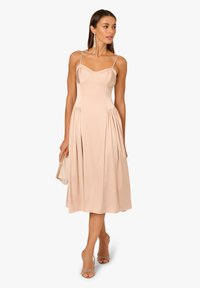 Blush-farbenes Midi-Kleid mit dünnen Trägern, figurbetontem Oberteil und plissierter Rock. Glattes Material, einfarbig, kombiniert mit einer neutralen Clutch und Absatzschuhen.