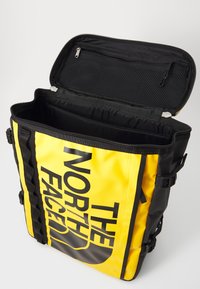 Zaino giallo e nero con un grande logo, scomparto con zip, tasca in rete e spallacci regolabili. Presenta un esterno impermeabile.